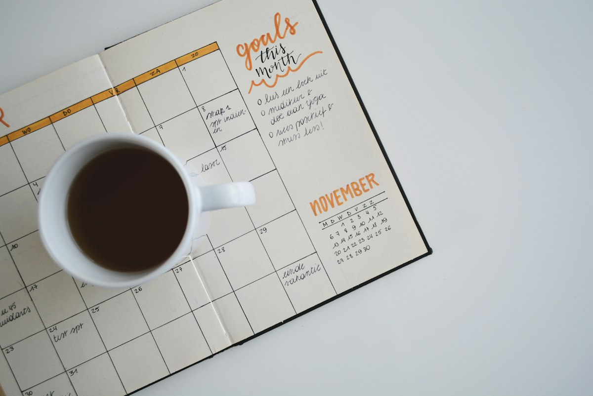 Desk calendar with dates marked, next to a pen and coffee cup