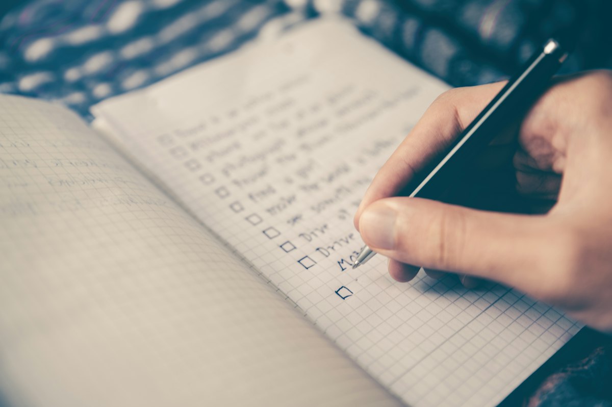 Person writing in a planner with a laptop open on the desk