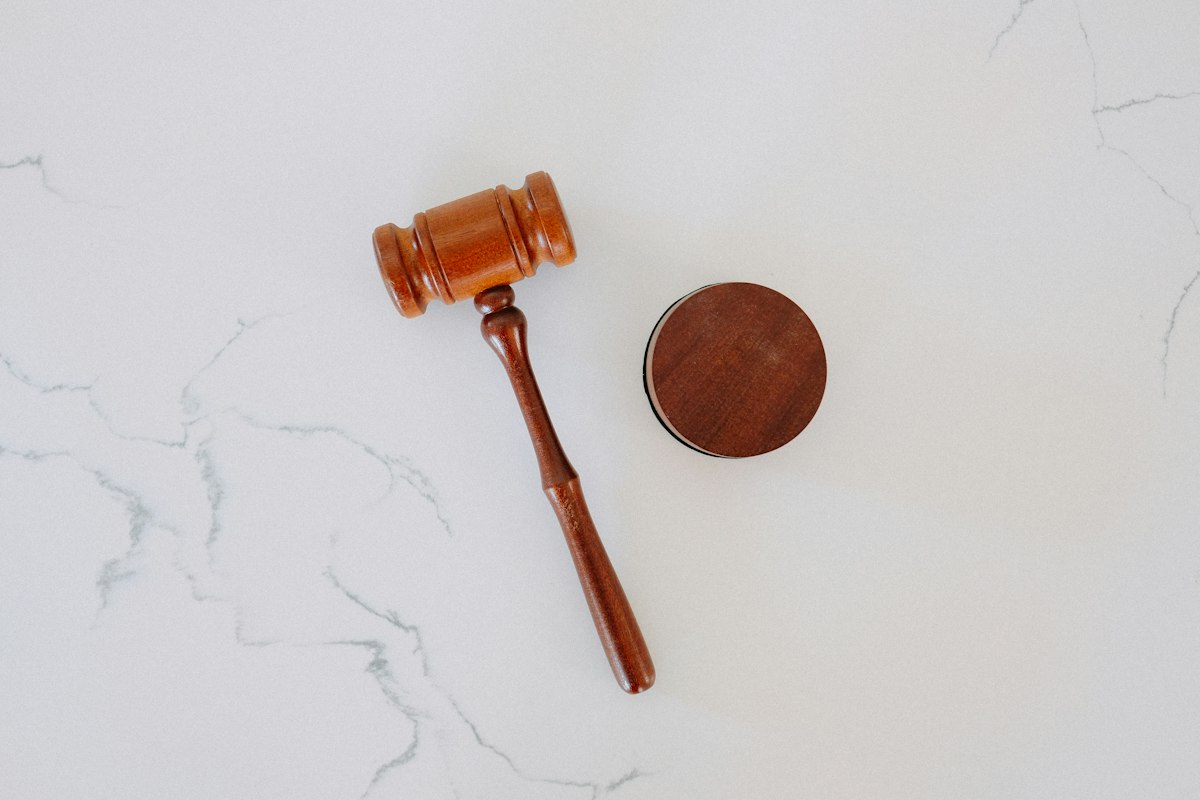 A gavel resting on a wooden desk beside legal documents and a pen